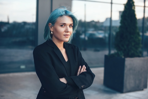 Belle femme aux cheveux bleus posant gaiement dans un costume contre un grand bâtiment