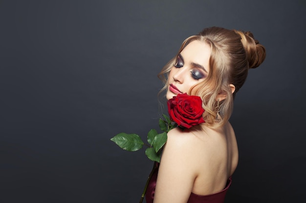 Une belle femme aux cheveux blonds et au maquillage tient des fleurs de roses rouges sur un fond noir
