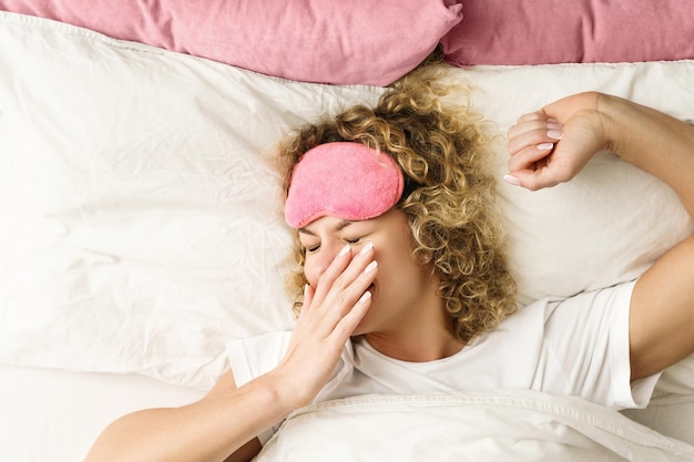 Belle femme aux cheveux bouclés se réveillant après un bon sommeil dans une chambre