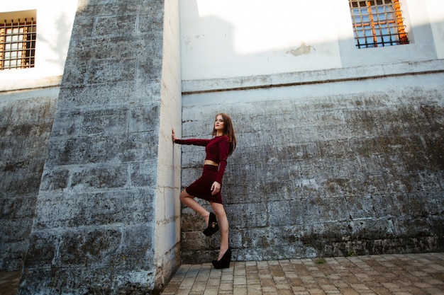 Belle femme aux cheveux bouclés vêtue d'une robe rouge fashion, debout contre le mur