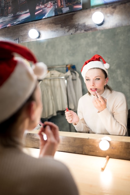 Photo belle femme aux cheveux bruns en pull blanc regarde dans le miroir de maquillage