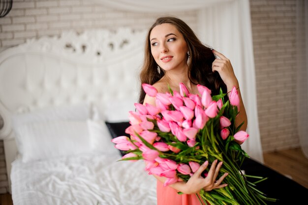 Belle femme aux cheveux longs, assise sur le lit avec bouquet de tulipes