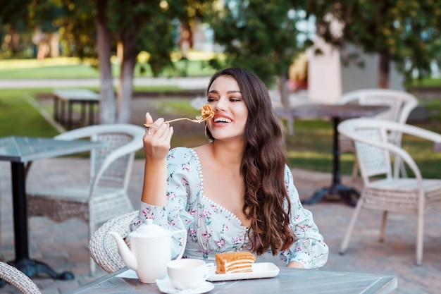 Photo belle femme aux cheveux longs mangeant un gâteau au miel dans le café en plein air en été