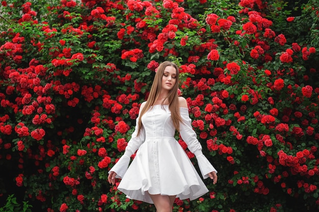 Belle femme aux cheveux longs et à la peau parfaite portant une robe posant près de roses en fleurs dans un jardin