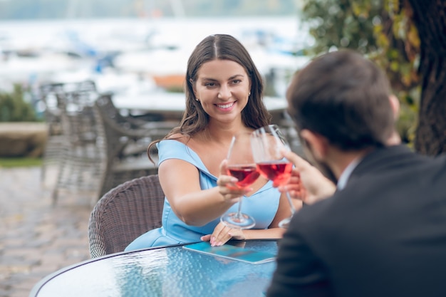 Belle Femme Aux Cheveux Longs En Robe Et Homme Assis Avec Des Verres De Vin Rouge à Table Dans Un Café En Plein Air