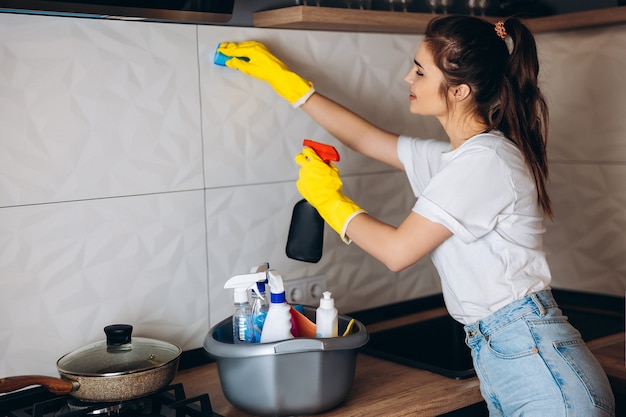 Belle femme aux cheveux noirs dans des gants de protection jaune nettoyage cuisine avec des détergents