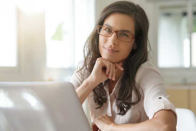 Belle femme aux cheveux noirs avec des lunettes travaillant sur un ordinateur portable