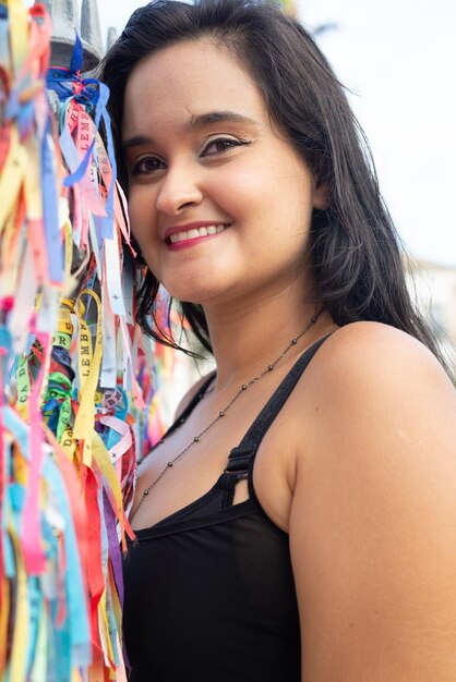 Photo une belle femme aux cheveux noirs souriante et regardant la caméra avec son visage pressé contre les rubans de souvenirs colorés