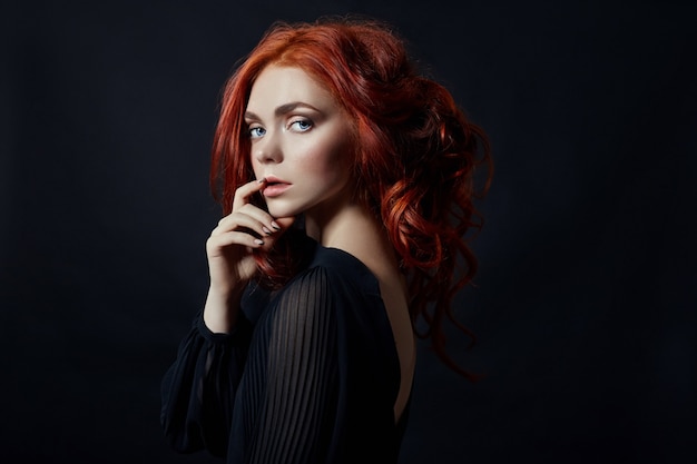 Belle femme aux cheveux rouges sur fond noir. Portrait d'une femme réussie, peau pure, maquillage naturel, visage de soins de la peau. Portrait de contraste d'une fille adulte