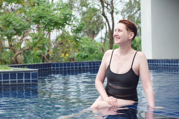 Belle femme aux cheveux roux courts se détend dans la piscine