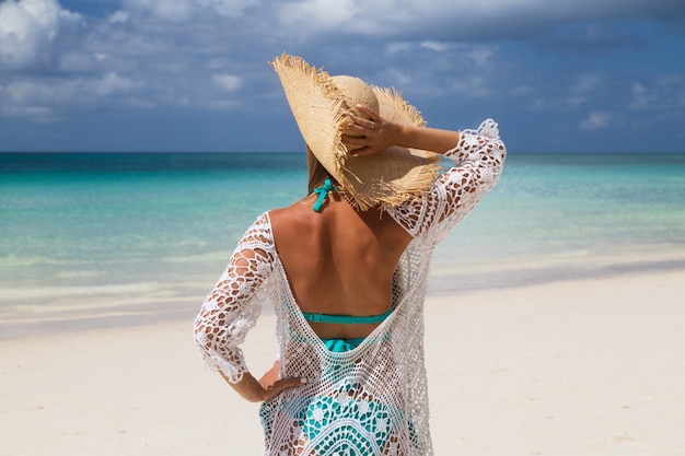 Belle femme aux longs cheveux blonds en bikini bleu sur une plage tropicale au sable blanc