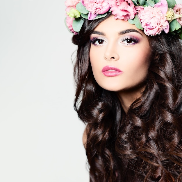 Belle femme aux longs cheveux bouclés maquillage parfait et couronne de fleurs de printemps