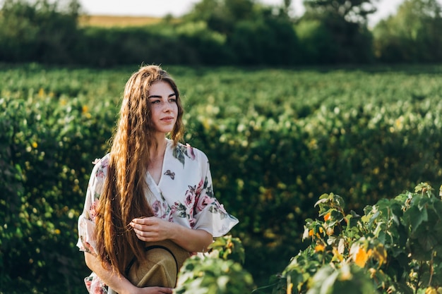 Belle femme aux longs cheveux bouclés et taches de rousseur face sur le champ de cassis. femme dans une robe légère se promène dans la journée ensoleillée d'été