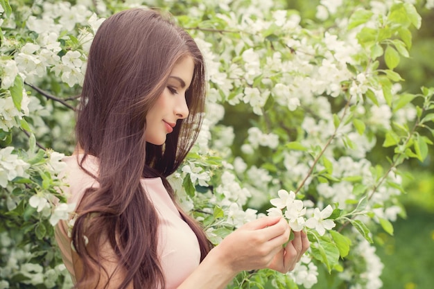 Belle femme aux longs cheveux bruns tenant des fleurs de pomme de printemps sur fond floral