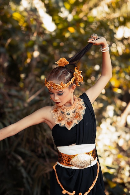 Belle femme balinaise tenant ses cheveux noirs tout en posant dans une robe de danse noire à l'intérieur de la jungle