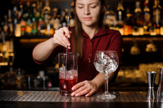 Belle femme barman en remuant une boisson alcoolisée sucrée avec de la glace