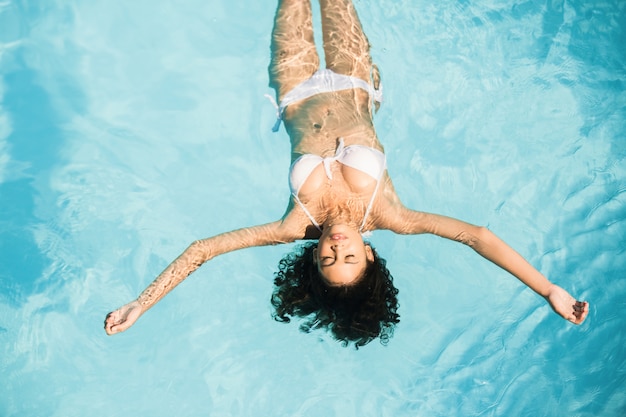 Belle femme en bikini blanc flottant dans la piscine