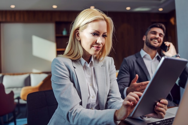 Une belle femme blonde en affaires porte à l'aide d'une tablette pour vérifier les médias sociaux des entreprises