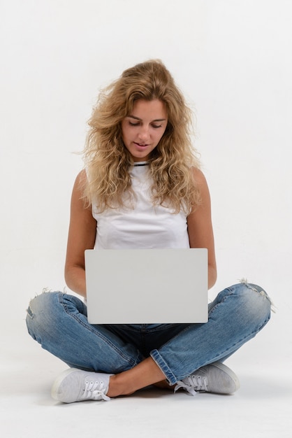 Belle femme blonde assise sur le sol avec un ordinateur portable sur blanc