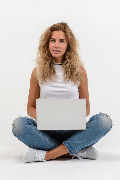Belle femme blonde assise sur le sol avec un ordinateur portable sur blanc