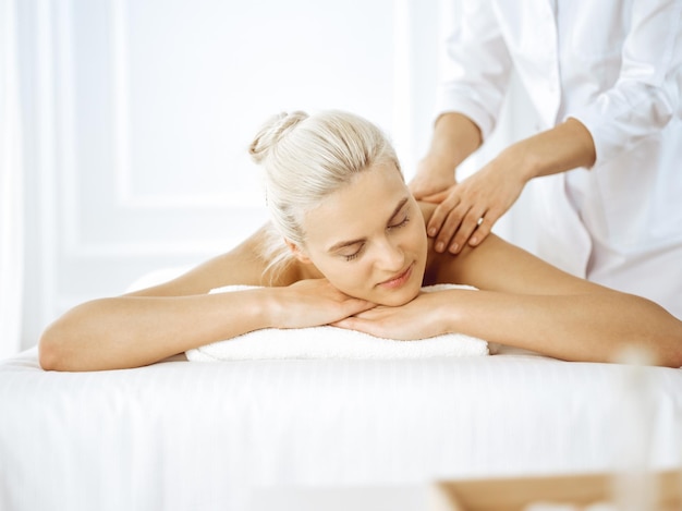 Belle femme blonde bénéficiant d'un massage du dos avec les yeux fermés. Concept de salon de spa.