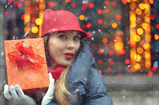 Belle femme blonde avec une boîte-cadeau au marché de Noël de rue pendant les chutes de neige. Espace libre