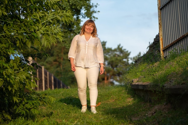 Une belle femme blonde avec un corps complet se promène dans un parc vert