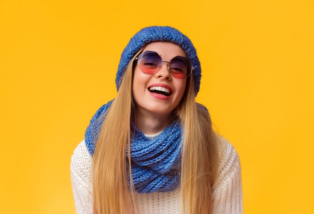 Une belle femme blonde dans un ensemble d'hiver et des lunettes de soleil riant sur un fond rose espace de copie