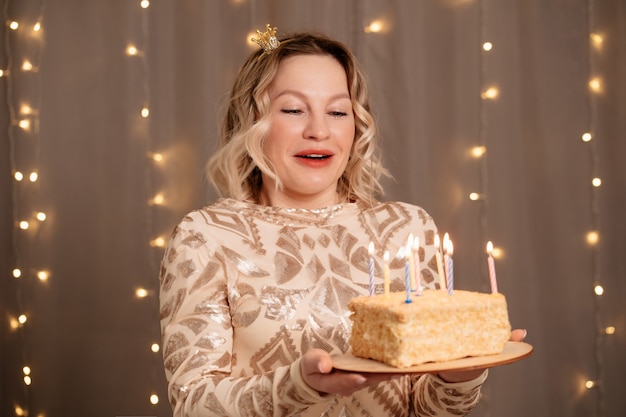 Belle femme blonde dans une petite couronne sur la tête avec un gâteau d'anniversaire et des bougies.