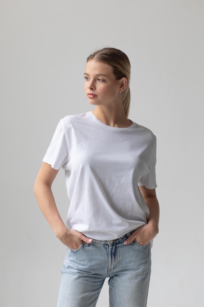 Une belle femme blonde dans un t-shirt blanc et un jean bleu posant sur un fond blanc