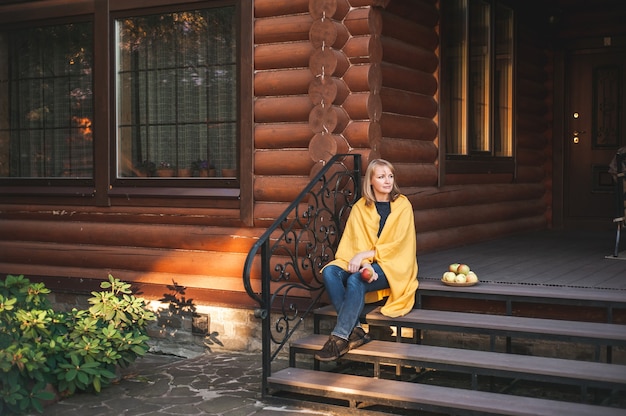 Une belle femme blonde est assise sur les marches du porche d'une grande maison en bois la femme est enveloppée...