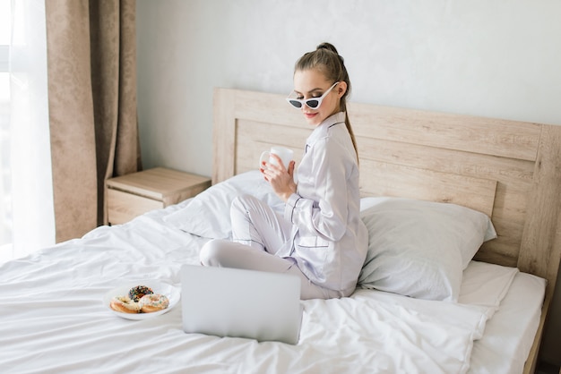 Belle femme blonde étudiant et travaillant dans un lit avec son ordinateur portable