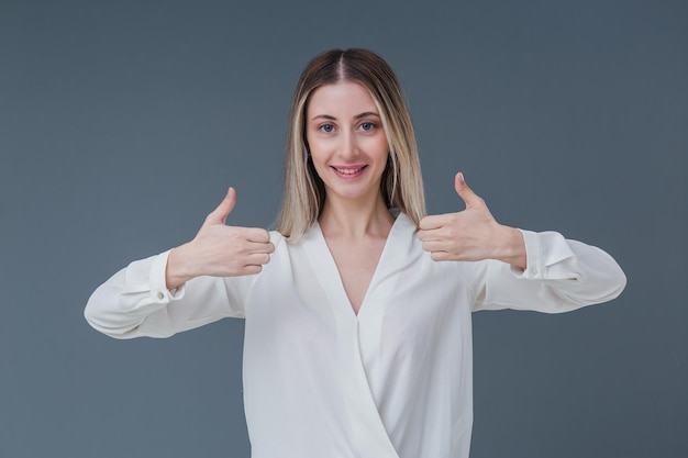 Belle femme blonde geste et concept de signe Elle fait un geste du pouce vers le haut avec un sourire chaleureux Comprend un espace de copie