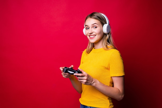 Belle femme blonde avec joystick et écouteurs sur mur rouge