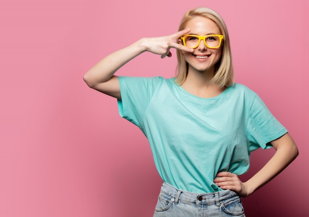 Belle femme blonde à lunettes jaunes sur mur rose