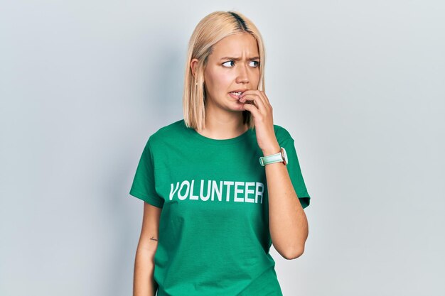 Photo une belle femme blonde portant un t-shirt de bénévole qui a l'air stressée et nerveuse avec les mains sur la bouche qui mord les ongles problème d'anxiété