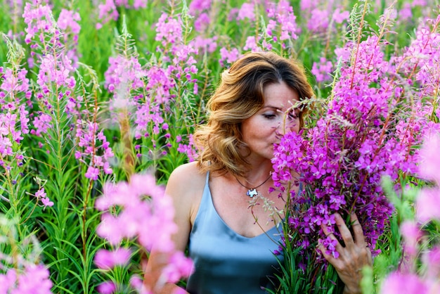 Belle femme blonde en robe grise se détend avec un bouquet de fleurs sur la prairie d'épilobe