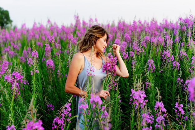 Belle femme blonde en robe grise se détend avec bouquet de fleurs sur la prairie d'épilobe