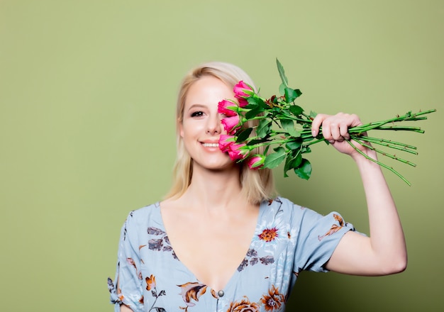 Belle femme blonde en robe avec des roses sur le mur vert