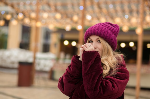 Belle femme blonde se réchauffe les mains sur le fond de la guirlande dans la rue à Kiev