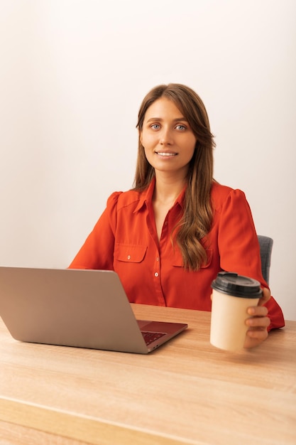 Belle femme blonde souriante à la caméra est assise derrière un bureau au bureau