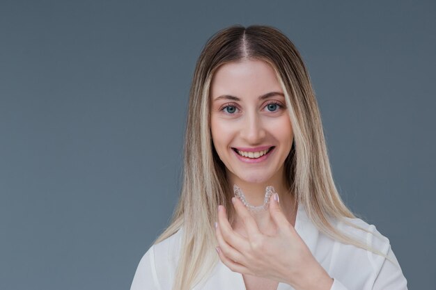 Belle femme blonde souriante tient un aligneur de dents invisible à des fins orthodontiques Comprend un espace de copie