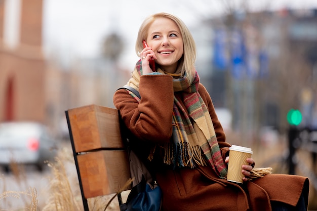 Belle femme blonde avec une tasse de café et un téléphone mobile