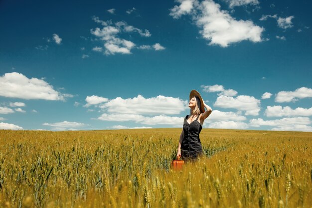 Belle femme blonde avec valise dans le champ de blé en journée ensoleillée