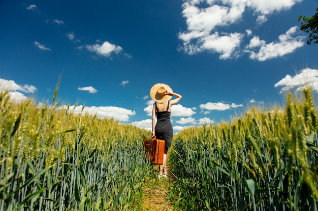 Belle femme blonde avec valise dans le champ de blé en journée ensoleillée