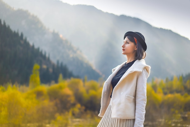 Belle femme en blouse blanche et chapeau noir posant sur fond de montagnes d'automne.