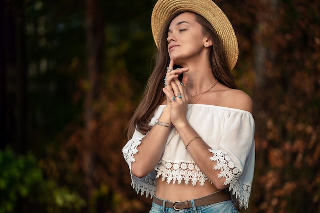 Belle femme boho chic à la mode en chapeau de paille et en blouse courte blanche avec des bijoux turquoise argent