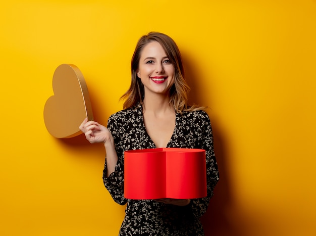 Belle femme avec boîte forme coeur sur mur jaune