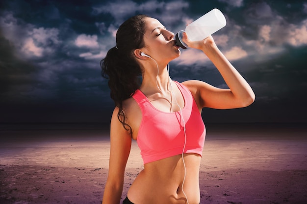 Belle femme en bonne santé buvant de l'eau contre un ciel nuageux foncé