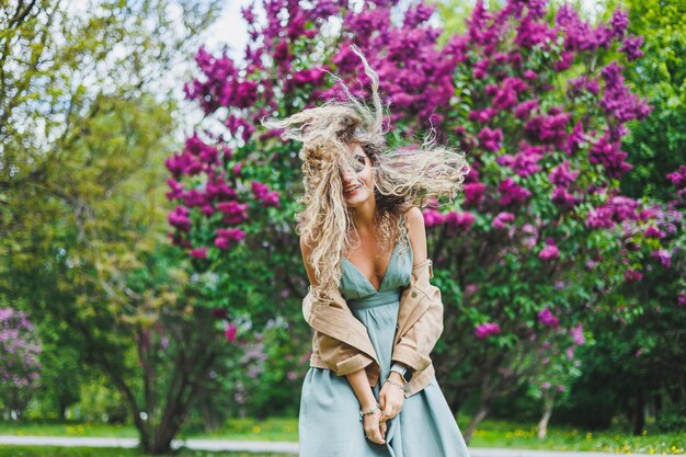 Une belle femme bouclée dans une robe d'été court et se réjouit qu'elle porte des lunettes de soleil sur fond d'un buisson de lilas violet